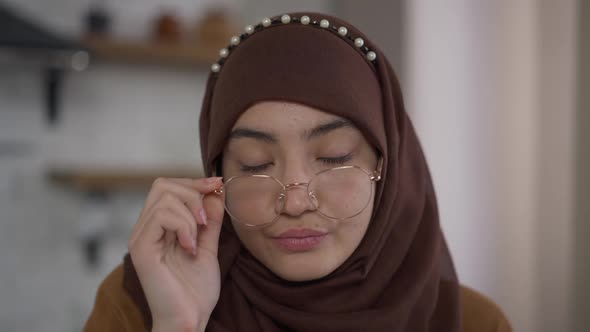 Headshot of Exhausted Middle Eastern Beautiful Woman in Hijab Putting Down Eyeglasses Looking at alt