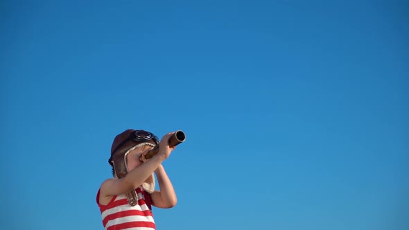 Happy child looking through vintage spyglass against blue sky. Slow motion