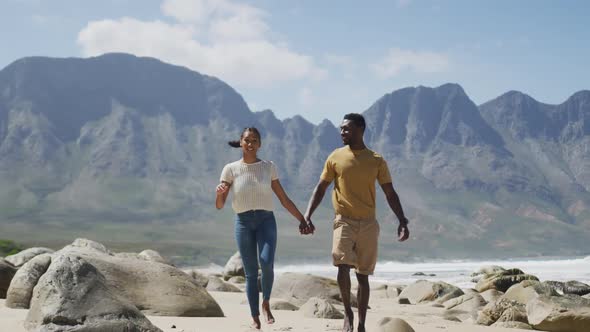 African american couple holdings hands and walking at the beach alt