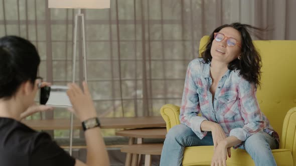 Model Posing Sitting on Couch at Home for Friend Taking Photograph on Phone alt