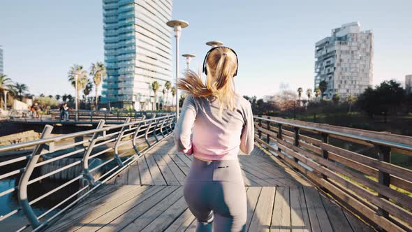 Young Caucasian Woman in Tracksuit Running Across Big City Bridge