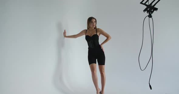 Attractive Young Woman in a Black Corset Standing with Her Hand Against the Wall, Looking Away From alt
