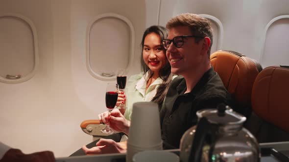 happy couple holding champagne glasses and cheers while traveling on airplane