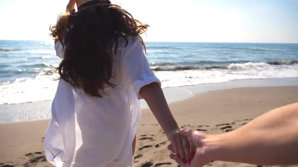 Follow Me Shot of Young Woman in Hat Pull Her Boyfriend on the Sea Shore alt