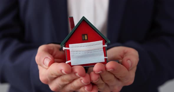 Businesswoman holding model of house with medical mask in hands alt