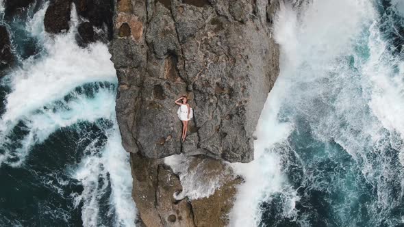 Woman in a White Short Dress Lies on the Edge of a Cliff