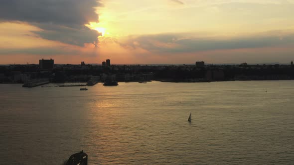 drone ascends, truck right up to golden sunset with ferry & sailboat on the Hudson River with New Je alt