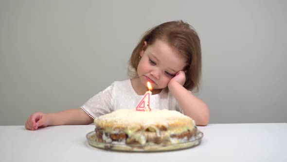 a Little Girl Looks at a Cake with Candles and Sad