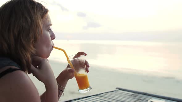 Young Woman Drinking Cocktail on the Beach at Sunset on Background