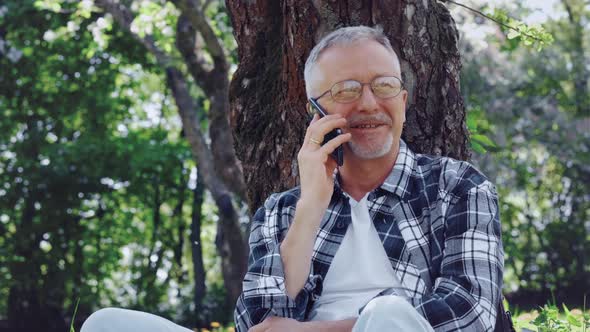 An Elderly Whitehaired Man with Glasses Talks on the Phone and Enjoys the Fresh Air and Nature