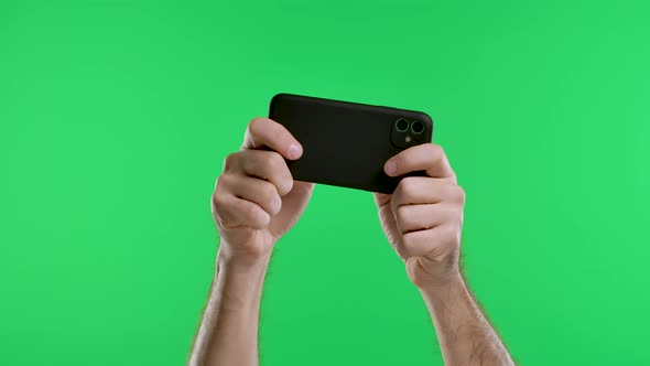 Male Hands Hold a Smartphone Horizontally Against the Background of a Green Screen Chroma Key alt
