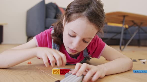 Girl playing and constructing with toy bricks on the living room floor alt