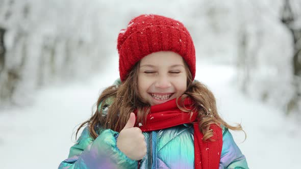 Smiling Little Girl With Thumbs Up Sign on Winter Background