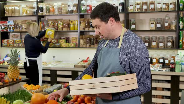 Male Store Clerk Puts Vegetables and Fruits in a Wooden Box