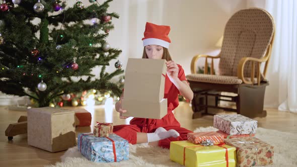 Wide Shot Portrait of Excited Teenage Girl Opening Christmas Gift and Smiling alt