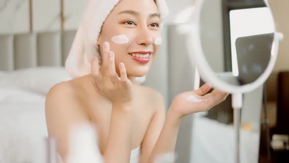 Happy attractive asian woman apply skincare cream on face and body. alt