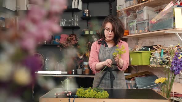 Woman Florist Prepares Flowers for Bouquet Tears Leaves in Shop on Wood Table. Ripping Leaves