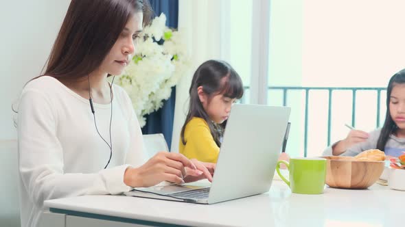 asian single mother working with laptop at home in living room with her daughter
