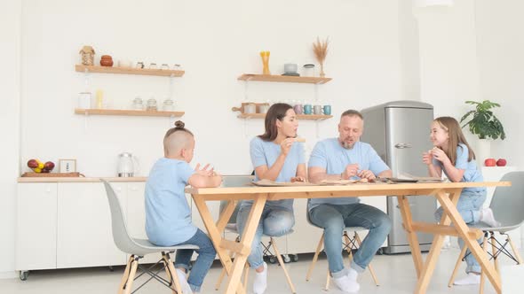 Young Family Deliciously Eating Italian Pizza Sitting in the Kitchen at the Table alt