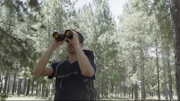 Hiker in forest looking through binoculars