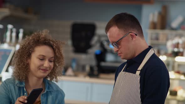 Caucasian waiter with down syndrome accepting contactless payment in the cafe from the client. Shot alt