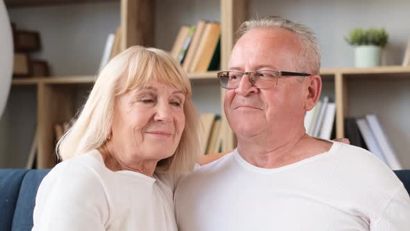 Closeup Portrait of Retired Couple Hugging While Sitting on Couch in Living Room alt