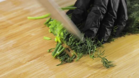 Chef's Hands in Gloves Are Chopping Greenery Dill and Onion on Wooden Board