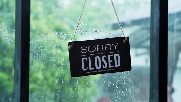 Asian little girl plays with an open sign hanging from a restaurant front door on rainy day. alt