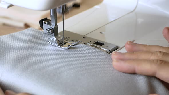 Woman hands with gray fabric sewing with a sewing machine. Women's hands sew on a sewing machine.