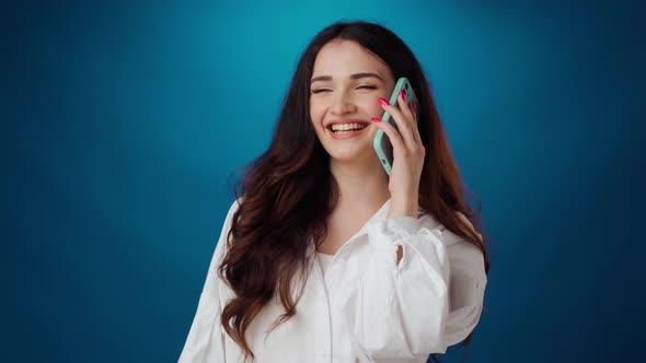 Young Curly Woman Talking on the Phone and Smiling Against Blue Backrgound