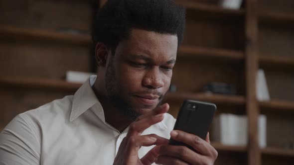 Young Adult Africanamerican Man Showing Negative Reaction on a Content Browsing on a Smartphone alt