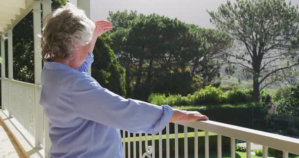 Smiling caucasian senior woman at home enjoying view of sunny garden from balcony alt