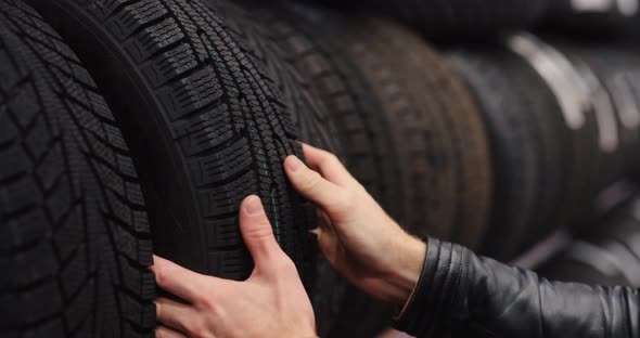 Man Touches Winter Car Tires in a Auto Shop alt