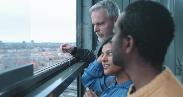 Mature realtor showing multi ethnic couple view from property window alt