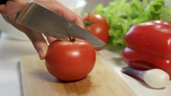 Female Hands Cut a Large Tomato with a Large Chef's Knife on a Wooden Cutting Board
