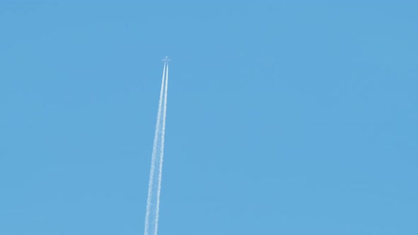 Distant Passenger Jet Plane Flying on High Altitude on Clear Blue Sky Leaving White Smoke Trace of alt
