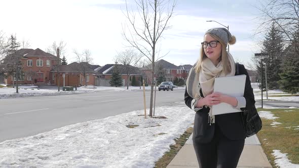 A Young Female Walking Outside In Winter Wearing A Scarf And Hat And Holding A Binder 1