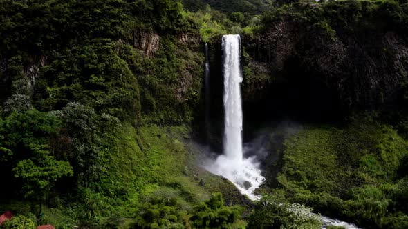 Aerial view, zooming in a a large waterfall until close to the water falling down and splashing alt
