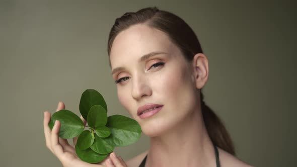 Beautiful young woman with soft and clean skin posing with tropical leaves.