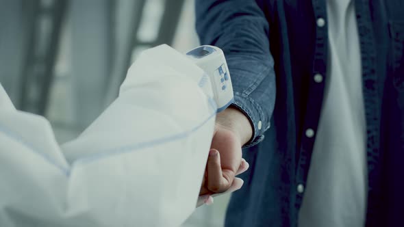 Unrecognizable Medical Worker Scanning Tourist's Hand With Thermometer In Airport alt