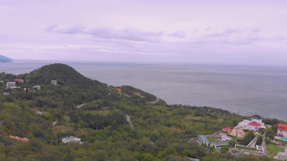 Flight Over Hilly Seacoast with Small Town Under Grey Sky