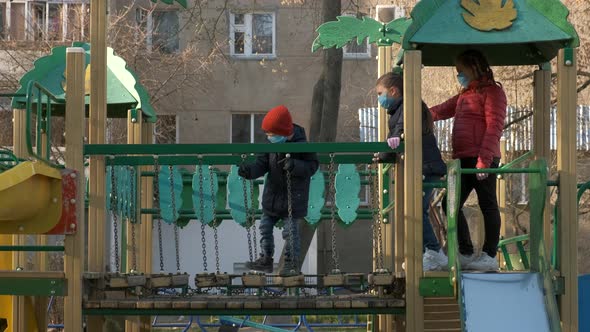Two girls and a boy in medical masks overcome an obstacle in the Playground