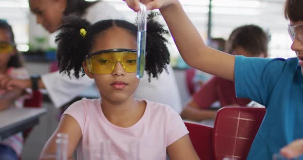 Diverse race schoolchildren wearing protective glasses holding test-tube during chemistry class alt