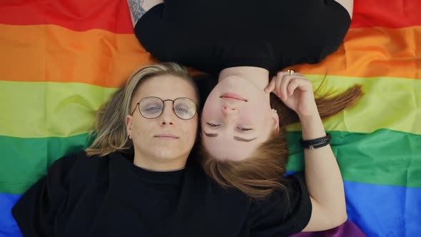 Pretty LGBT Couple Lying on Rainbow Flag and Looking at you alt