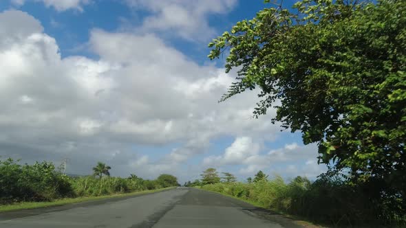 POV Driving Along Two Lane Road on Tropical Island Against Blue Sky and Clouds