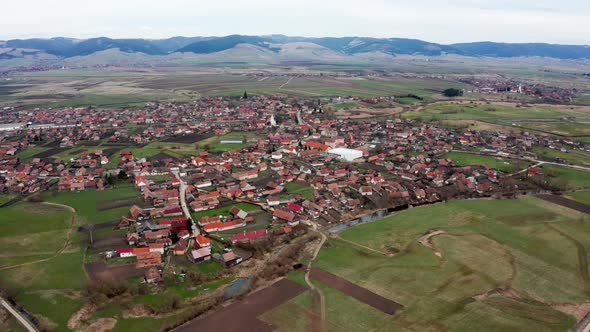 Aerial forward tilt down over Sansimion village and Ciuc Mountains in background. Romania, Transylva alt