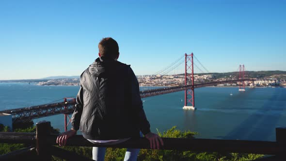 Sightseeing Man Tourist Looks at Ponte 25 De Abril and Tagus River in Lisbon alt