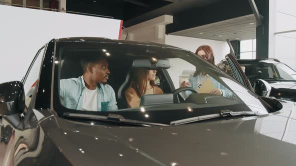 Beautiful Multiracial Couple Sitting Inside Modern Luxury Car and Examining