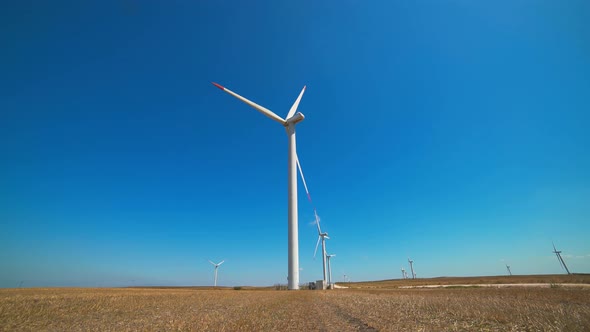 Renewable Wind Power Plant Turbines in a Flat Treeless Brown Field Under Cloudless Clear Sky