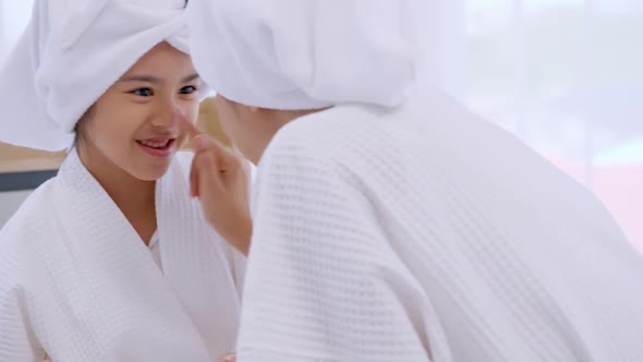 Mother with little daughter in bathrobes doing beauty treatment together at home. alt